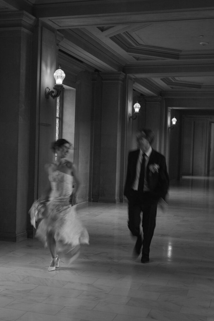 Black and white image of bride and groom running down the San Francisco City Hall