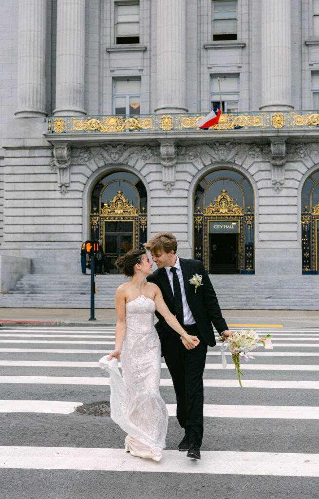 Bride and groom crossing the street while looking at each other and holding hands